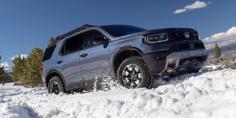 2027 Honda Passport TrailSport Elite in Smoke Blue Pearl front driving through deep snow (Mid-Size SUV).